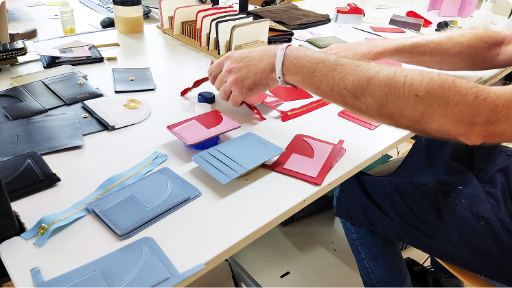 Craftsman assembling leather accessories and wallets on a workbench with various colorful pieces.