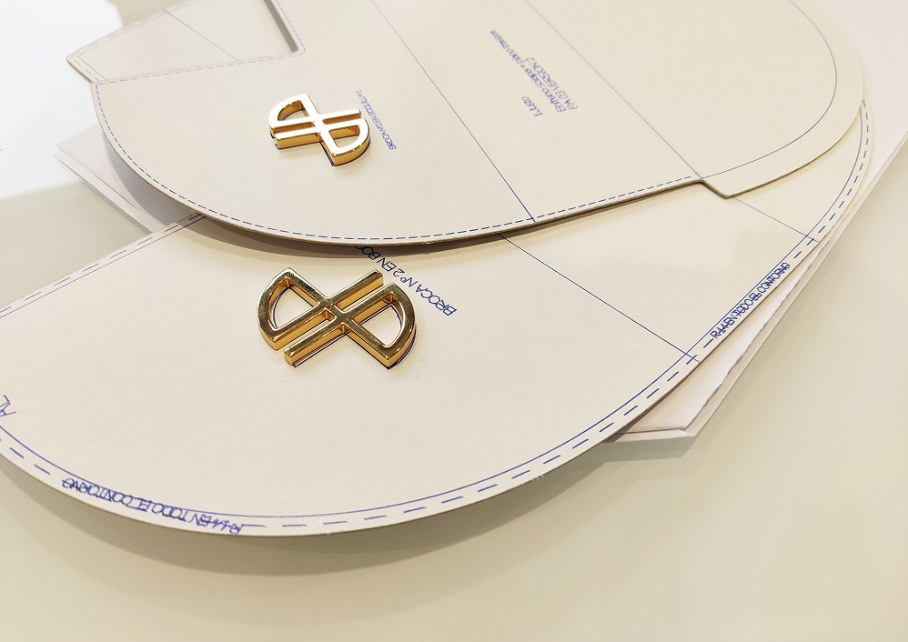 Leather bag design templates with golden metal logo pieces placed on top of the pattern sheets.