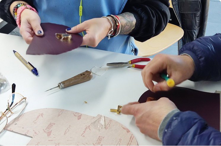 Close-up of two artisans attaching metal hardware to leather pieces during the bag assembly process.