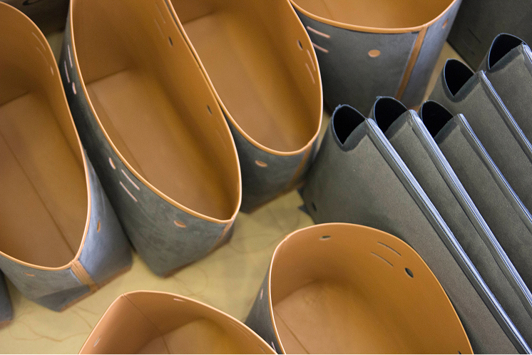 Pre-assembled leather bag bodies lined with tan interiors arranged in rows before final assembly.