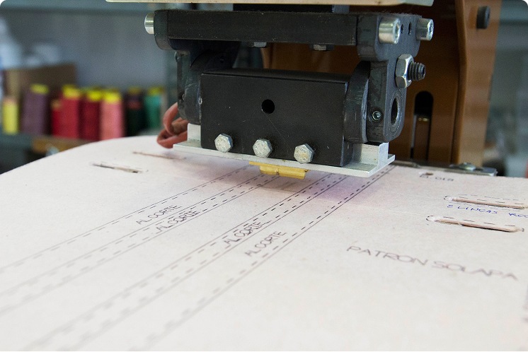 Cutting machine working on leather bag patterns marked with lines and measurements.
