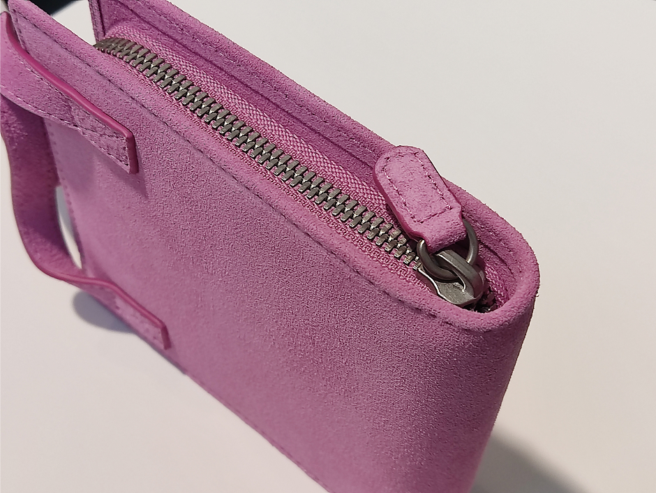 Close-up of a pink suede handbag showing the zipper and stitching details on a light background.