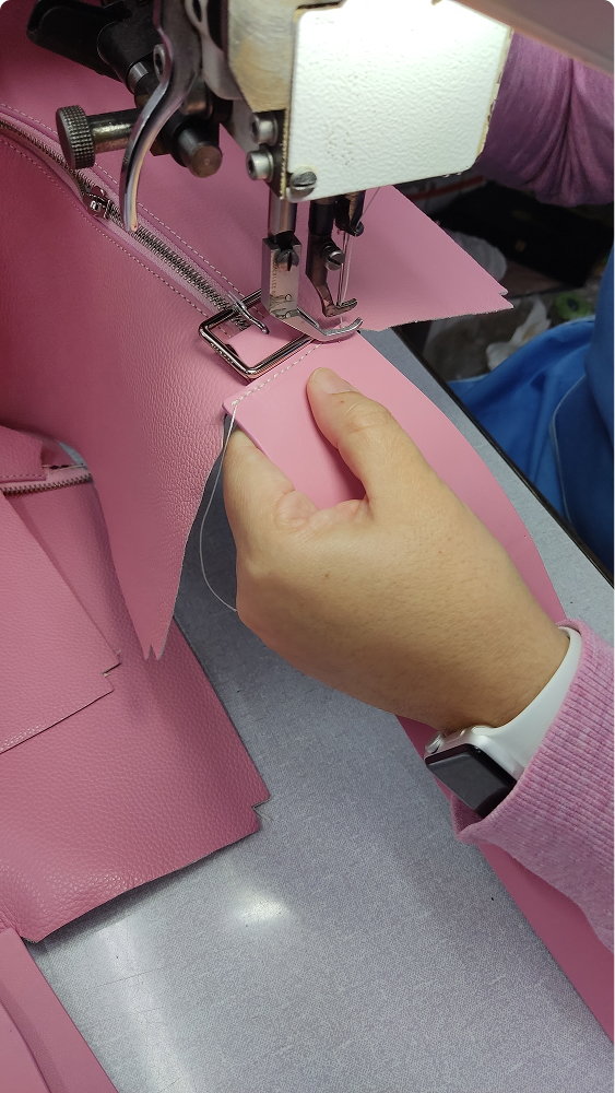 Artisan sewing a pink leather handbag on an industrial sewing machine, focusing on precision stitching.